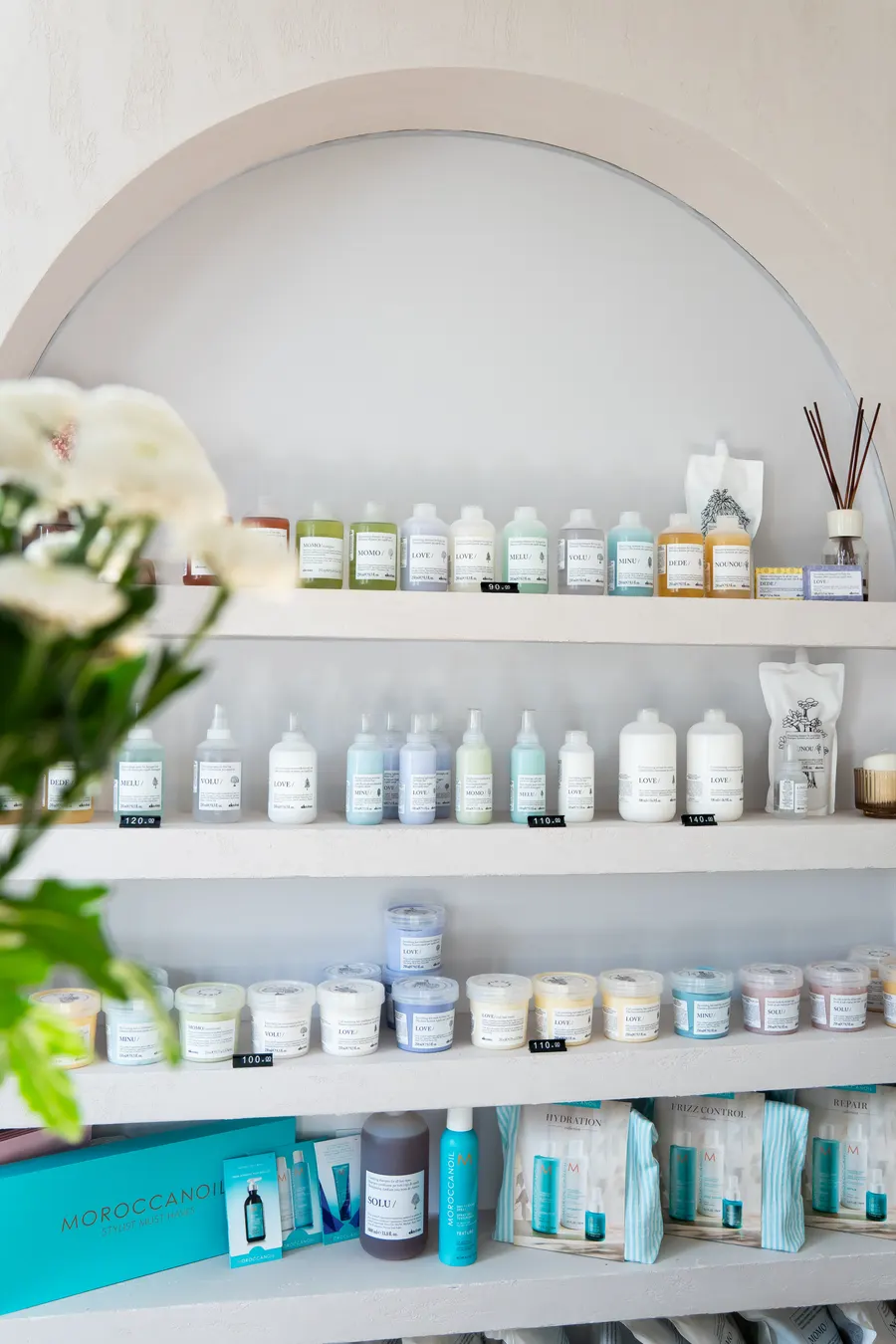 Półki w łukowej wnęce z kosmetykami do włosów Davines i Moroccanoil